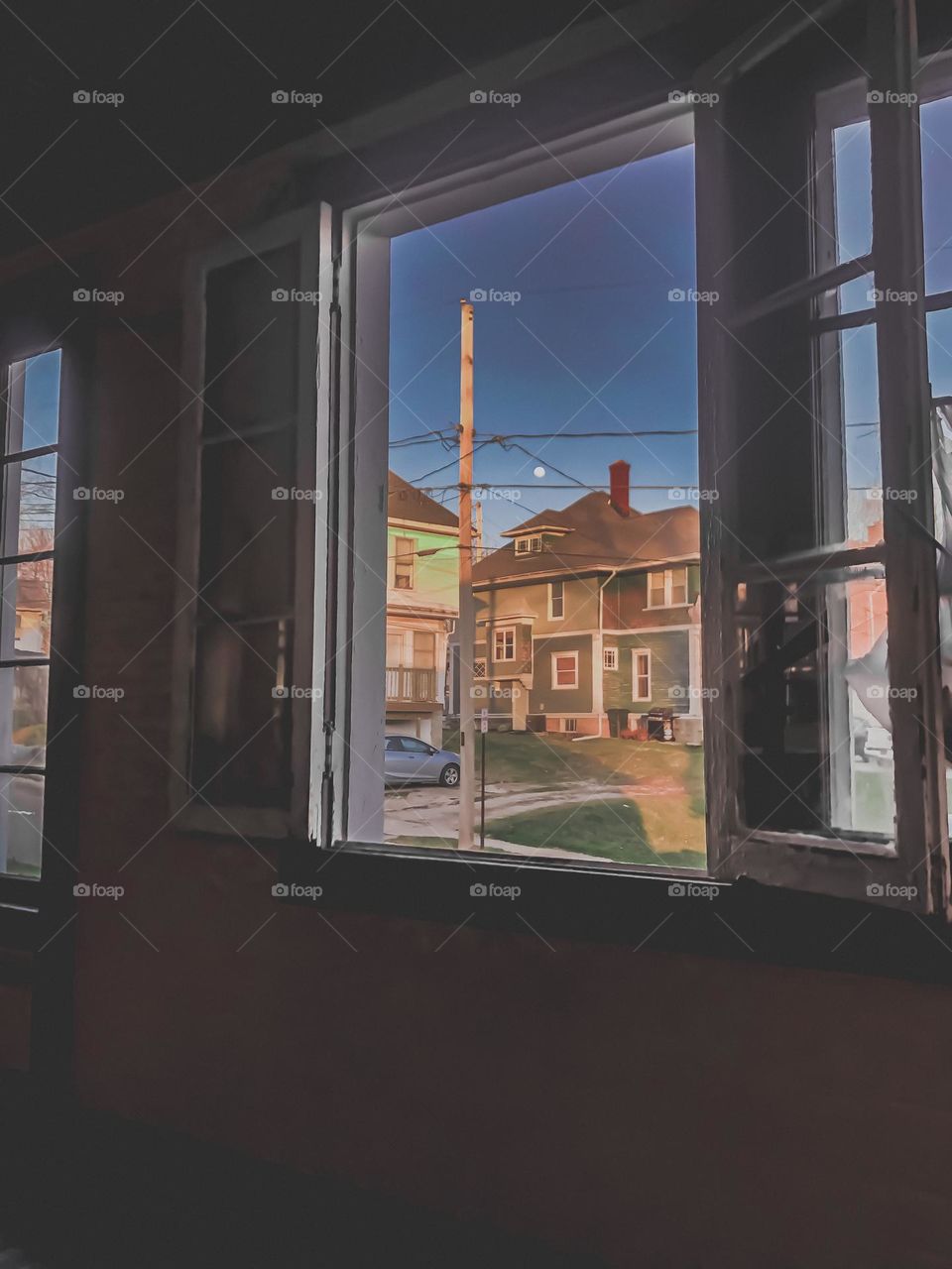 Windows of a porch looking out to the neighbors and the street with a night time moon just coming out 