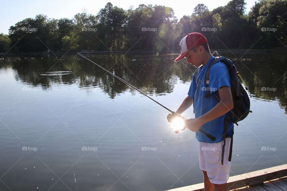 Boy fishing for bass in pond with sun reflecting off water in Summer