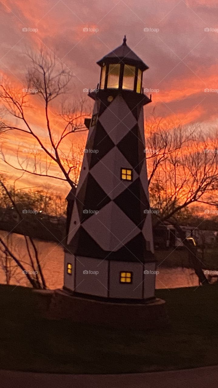 Sundown Completed Sky is opening up. Blistering Orange Slivers along with Yellows upper atmosphere bleeding down to the lower with Grays Blues Violets tops of high clouds getting into the act by opening up. Lighthouse standing firm