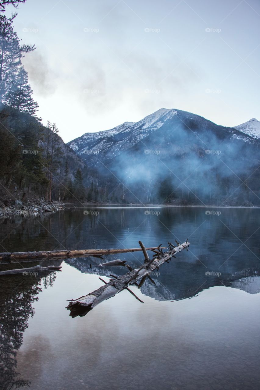 The reflection of snowy mountain peaks on a cold, fog covered lake at dawn. 
