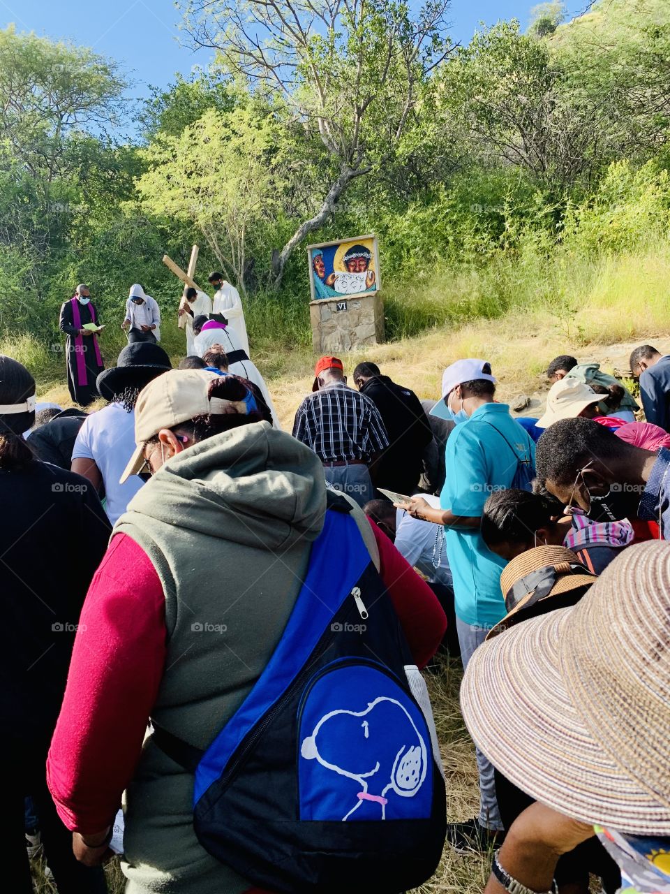 A group of pilgrims bowing in prayers on a pilgrimage of the way of the cross. With a priest carrying the cross at one of the stations of the way of the cross.