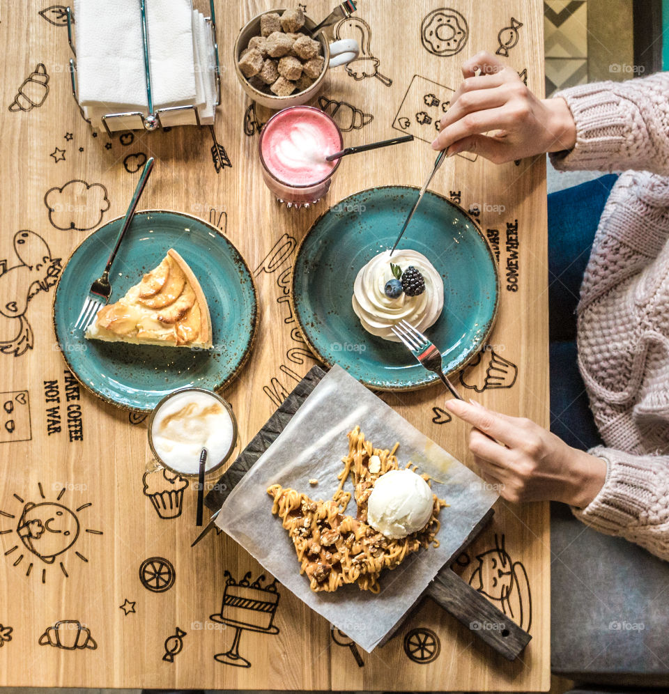 cafe table with pastries and female hands, view from above