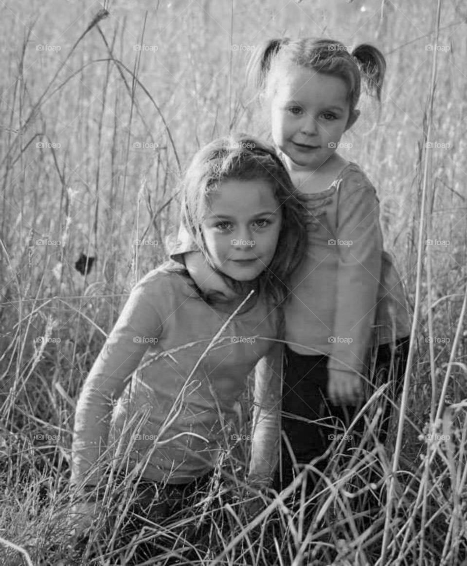 Two young sisters standing together in a hay field illuminated by the setting sun. Family quality time.