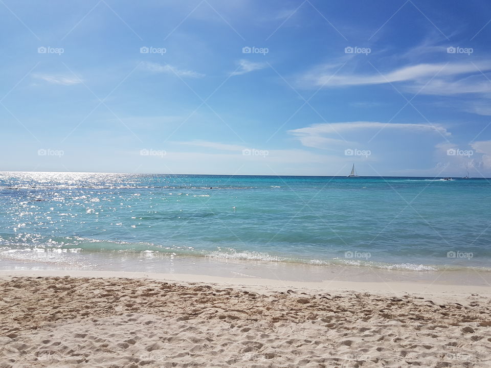 stunning serene ocean shoreline with colors of aquamarine, blue, turquoise, navy. Sandy beach with ocean tide and blue sky on sunny vacation day in Dominican Republic