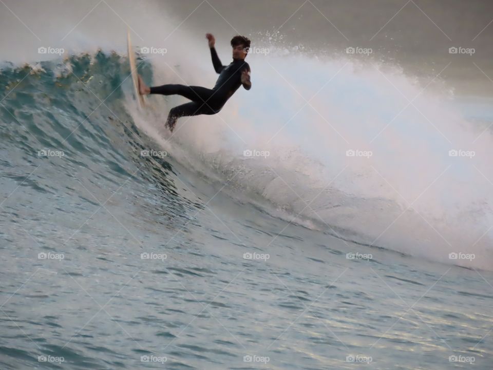 Summer by the ocean: surfer doing tricks up and down the wave at sunset on the Australian coast.