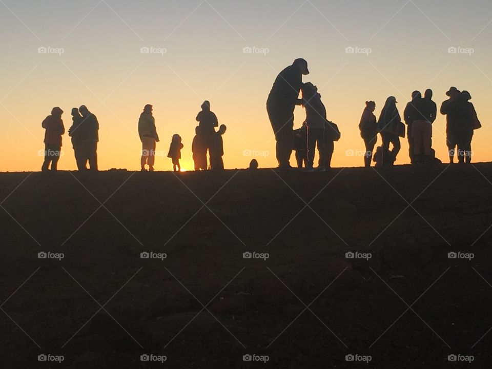 A group of people gathered together silhouetted by the sunset they are watching.