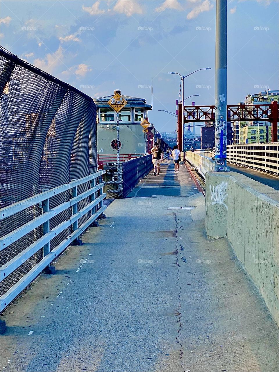 This is the pedestrian lane leading across the „Pulaski Bridge“ at „Newtown Creek“ walking from „Greenpoint“, Bklyn to LIC, Queens. The setting sun gives the area a nice warm golden glow. 2023. Hypnotic Productions