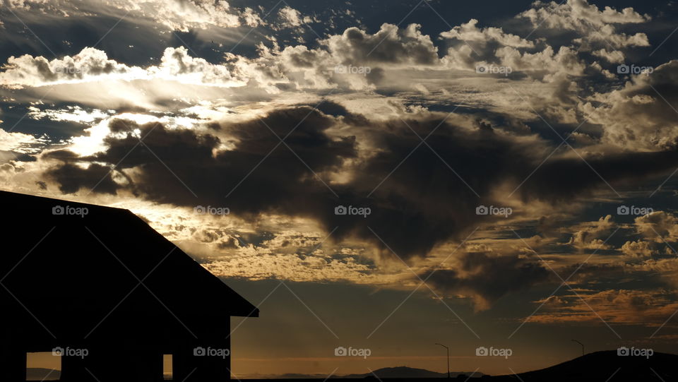 A moody sky created by clouds obscuring  the sunset over an abandoned structure.