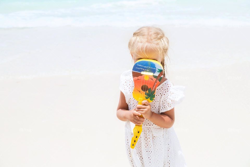 Little Caucasian girl playing on small guitar on beach 