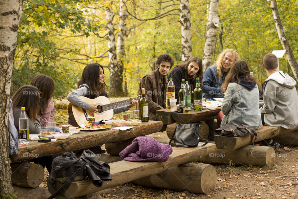 Friends meeting at the forest park, playing a guitar