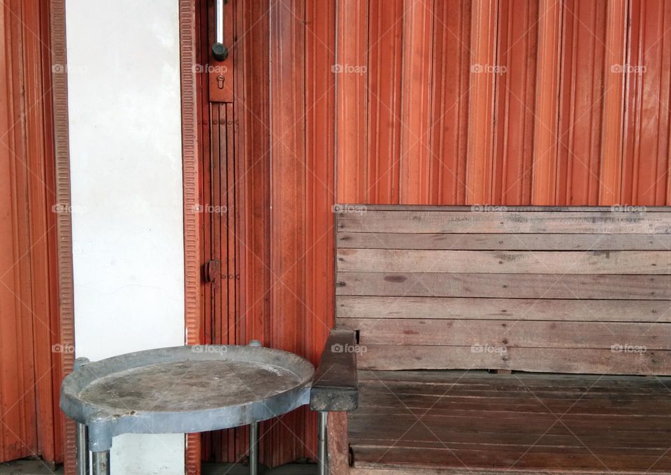 wooden bench and metal round table against the rolling door in orange color. lines pattern