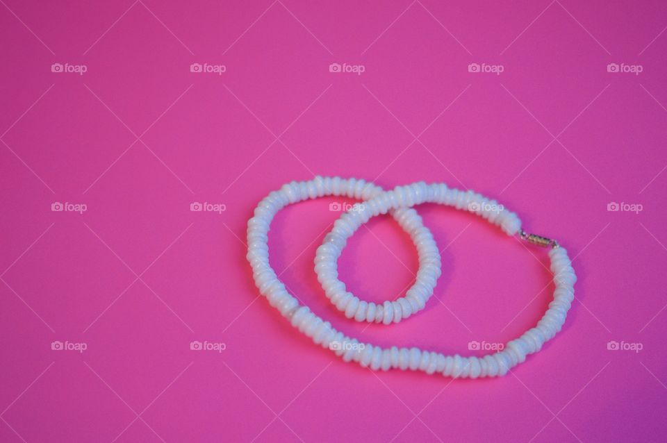 Contrasting flatlay on a bright pink background with a white shell necklace 