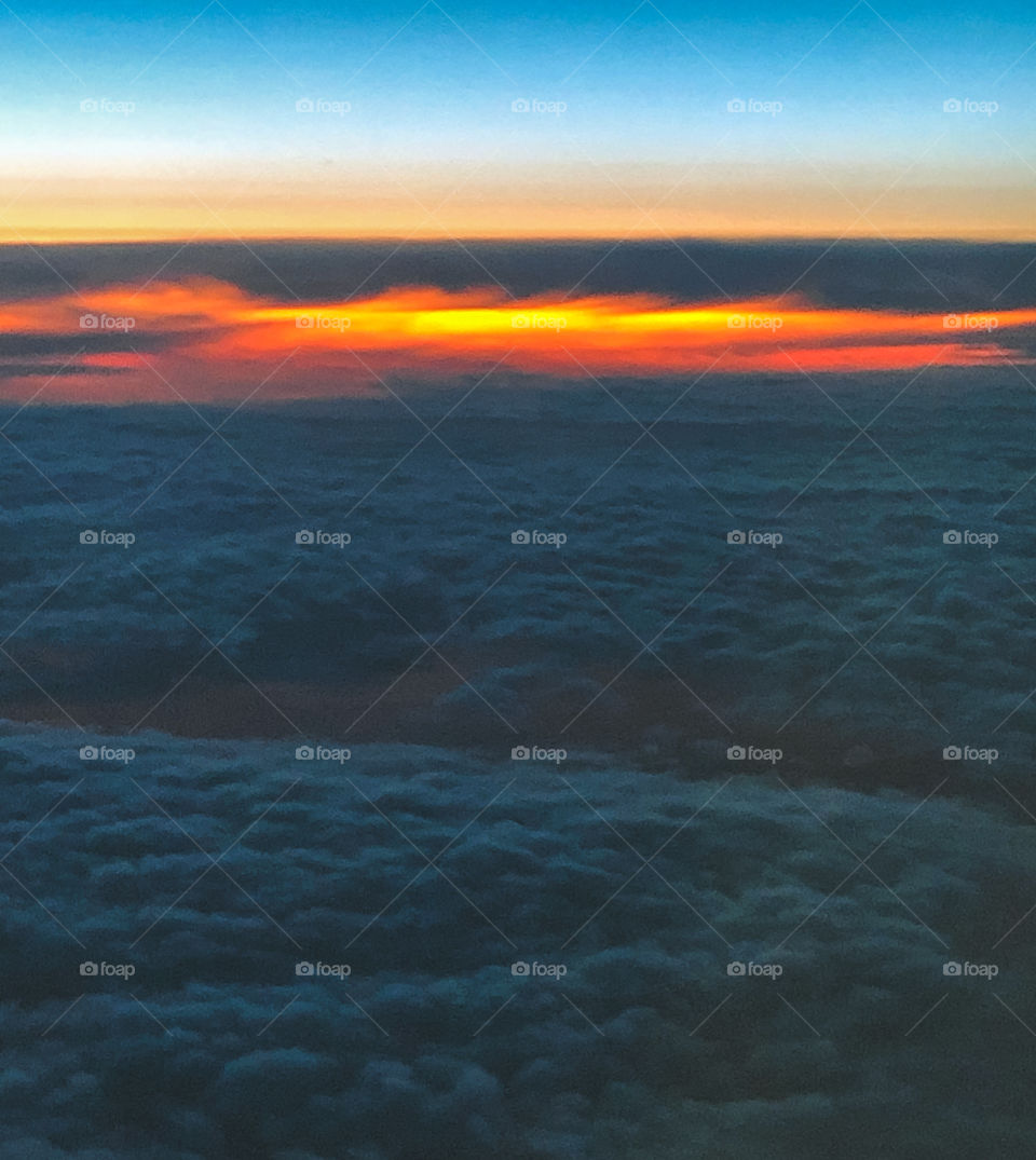 A sea of blue clouds leads to an orange sunset as viewed from a plane