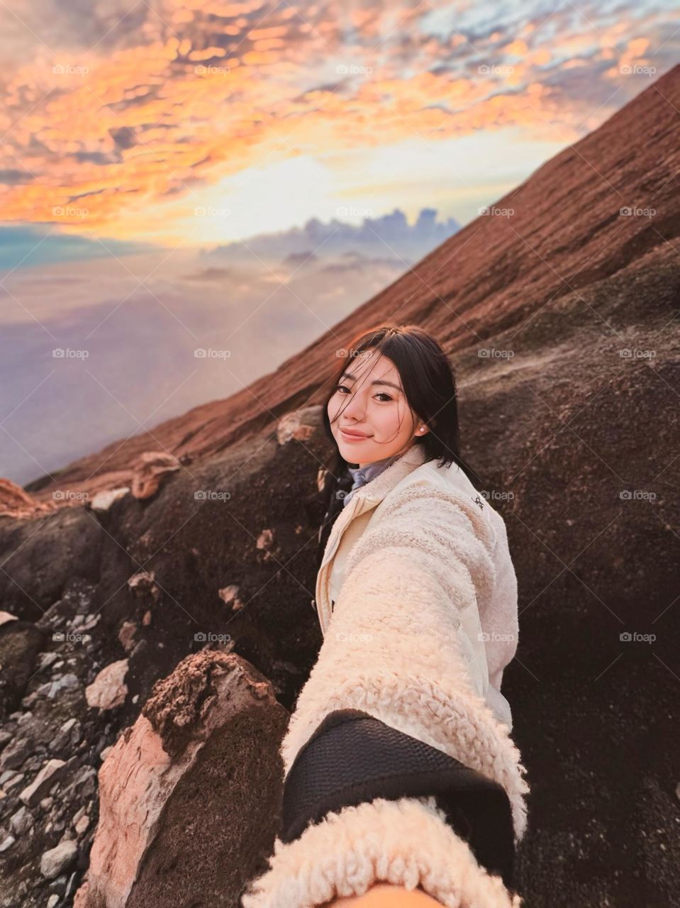 Portrait of a young woman taking a selfie on a mountain slope with a beautiful evening sky in the background