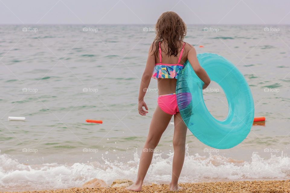 Back of child girl on sea beach with inflatable tube in summertime