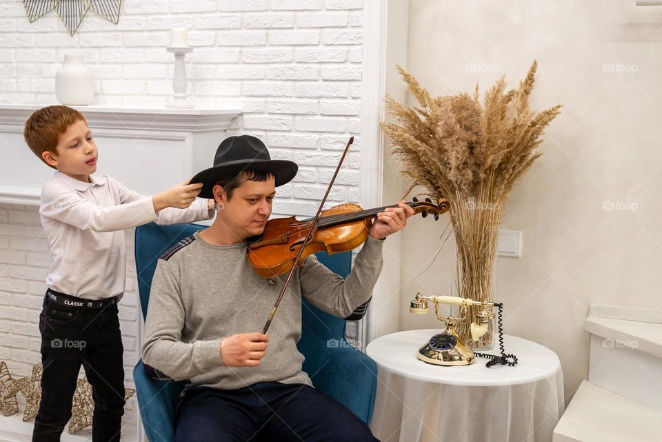 a young man plays the violin in a bright room, his son listens to music