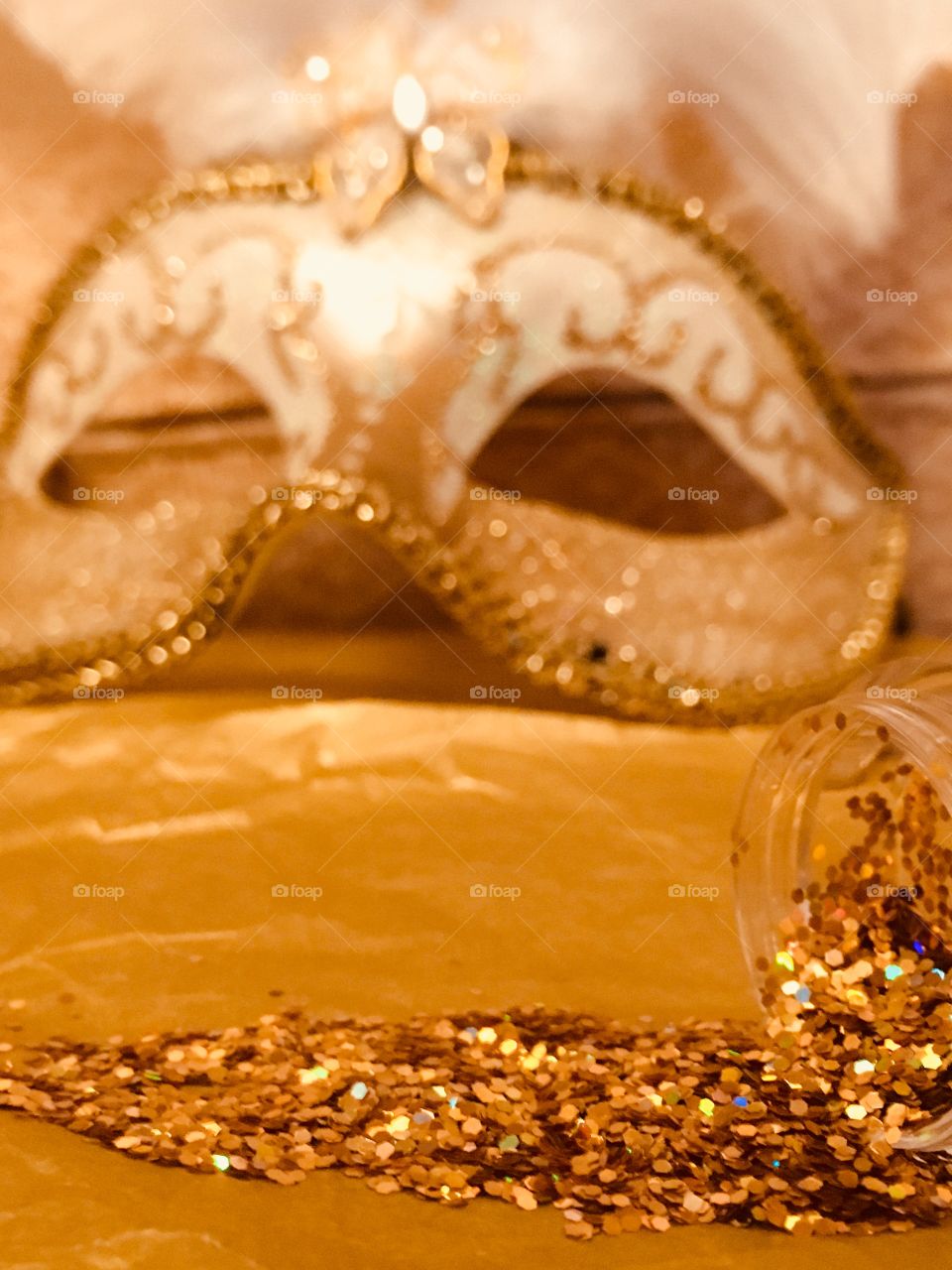 Gold glitter spilled onto gold tissue paper with a gold Venetian masquerade mask 