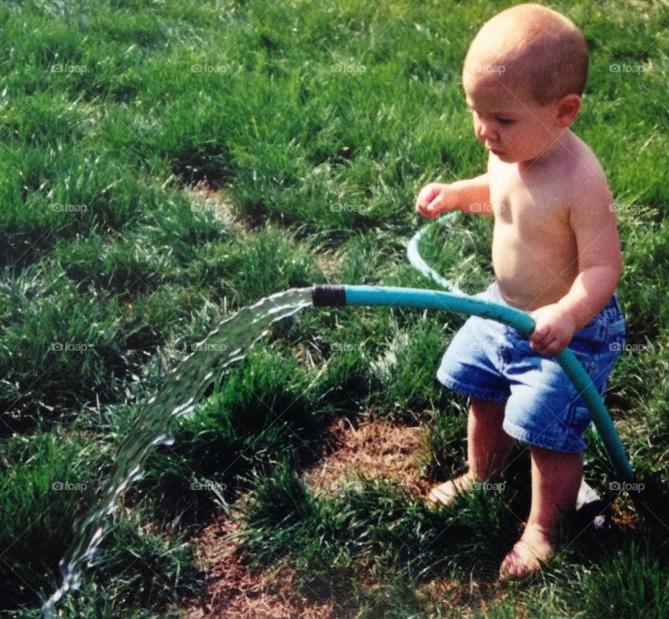 Toddler boy holding water hose