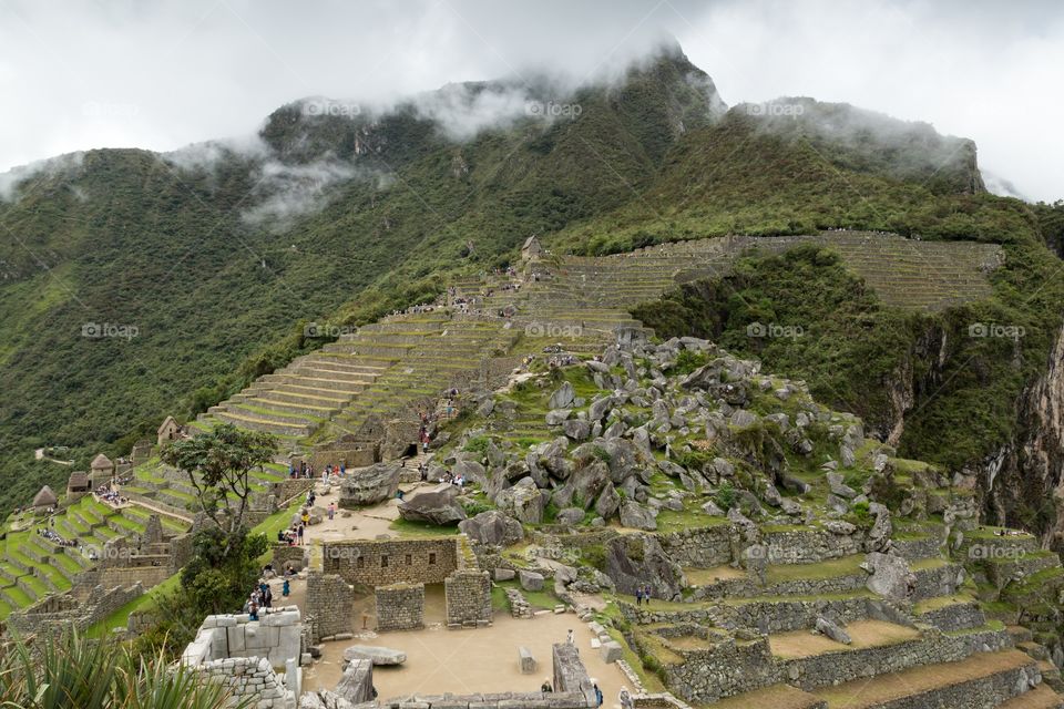 Machu Picchu ruins and terrace. View towards the entrance of Machu Picchu and farming terraces. Mountain peak behind cloud. Ruins in the foreground