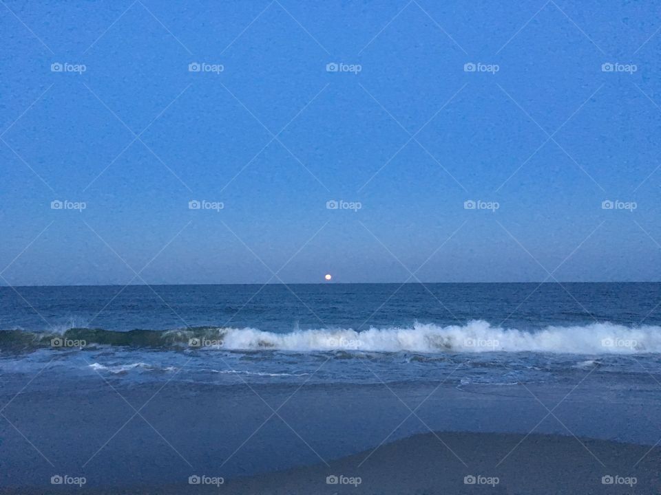 At the beach while the moon rises from the east.