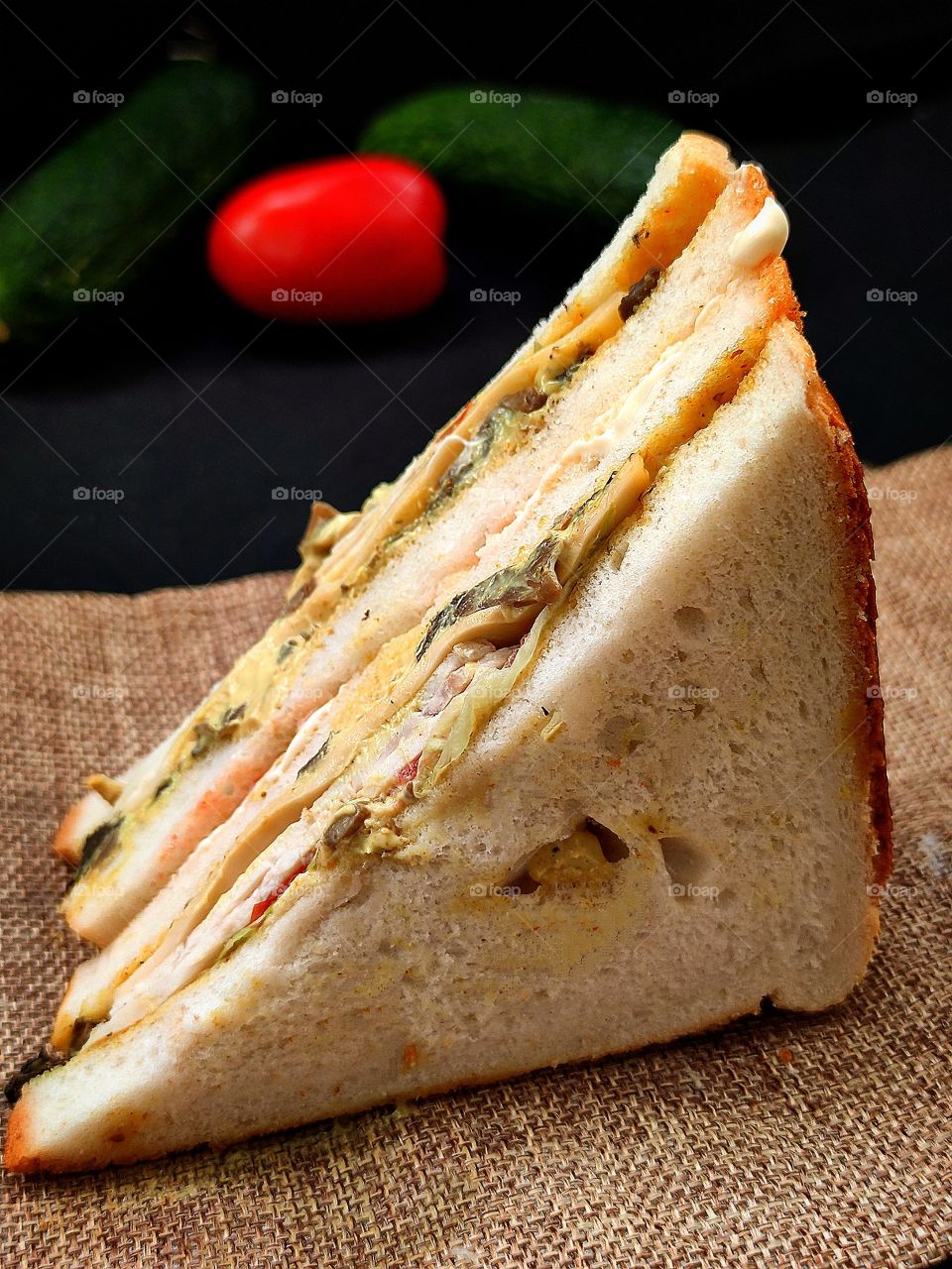 Sandwich: white bread, cheese, ham, tomatoes, lettuce, curry sauce.  In the background a tomato and two cucumbers