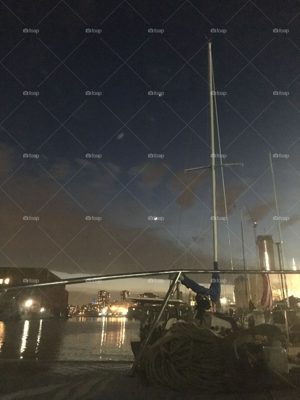 Aboard our sailboat, the “Salvation” late at night viewing the waters of the East River at Newtown Creek, Long Island City, Queens, New York and the illuminated cityscape in the far distance reflecting in it. Photo 2018. Hypnotic Productions