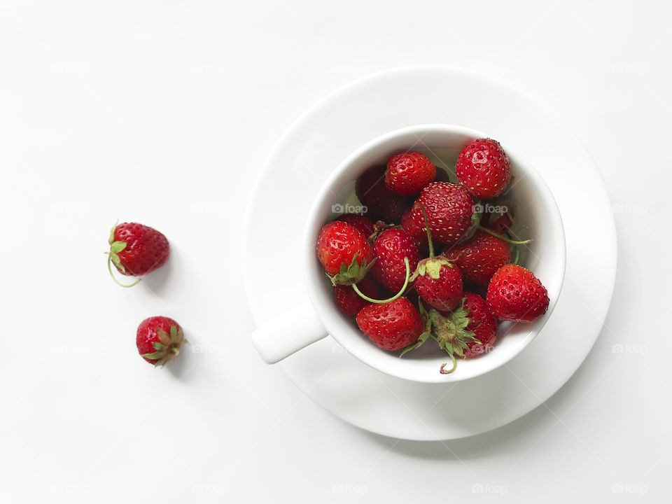 Red ripe strawberries in white cup on white saucer on white background 