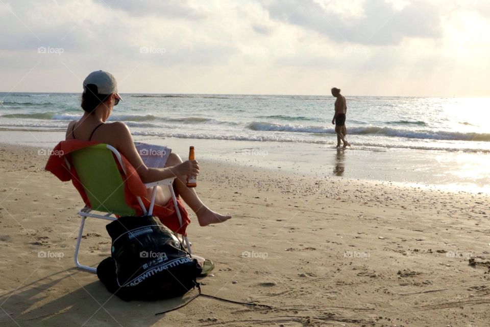 Mother having a break with a bottle of beer on the beach