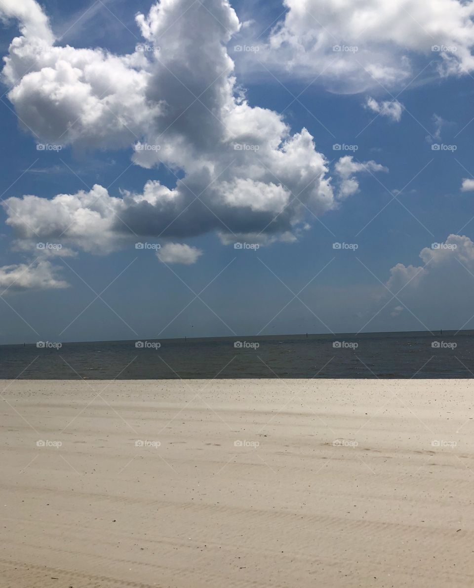 A gulf shore beach scene with puffy clouds, blue sky sand and water. 
