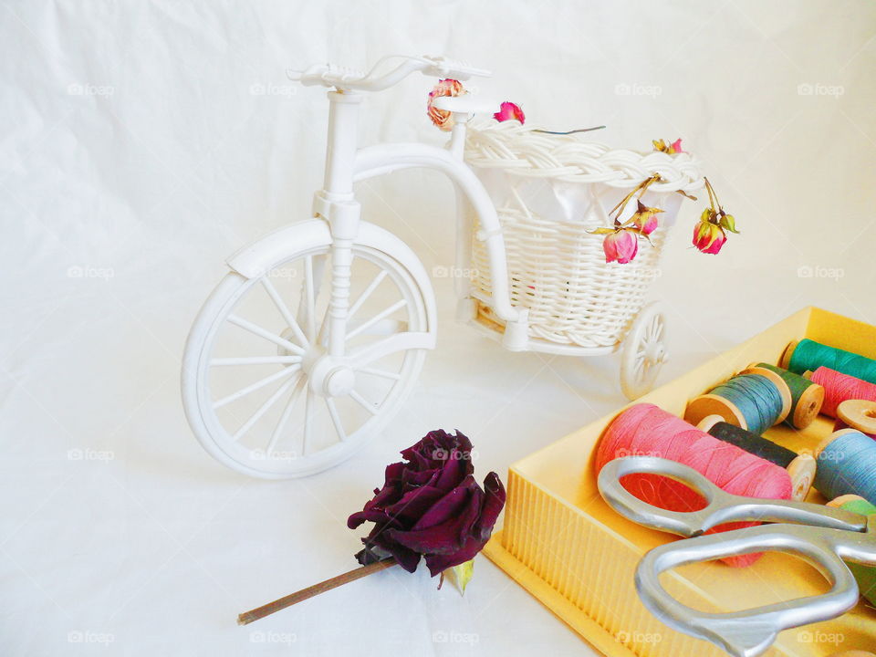 decorative toy bike, dried rosebuds and thread on white background