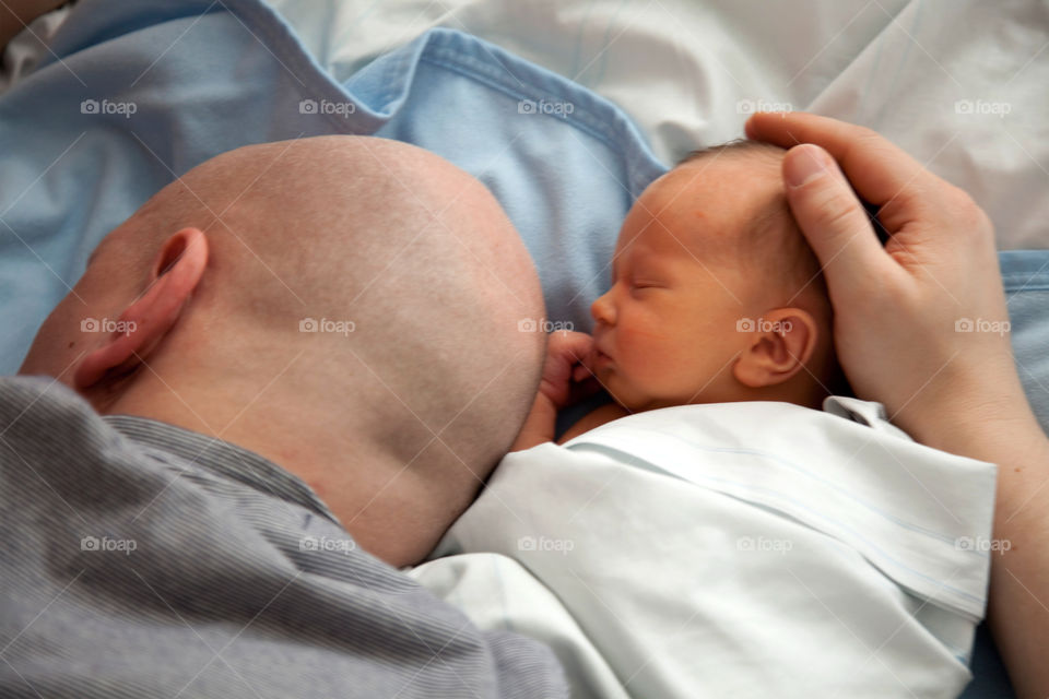 Father with newborn baby sleeping on bed