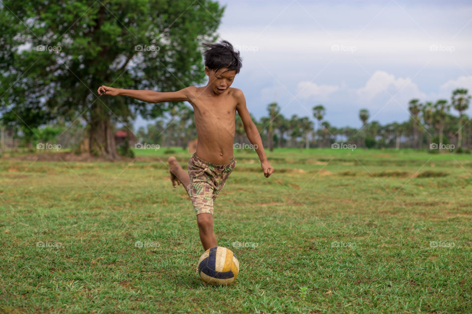 A boy run to kick a ball. I saw a kid run to kick a ball to his friend who is a goal keeper.