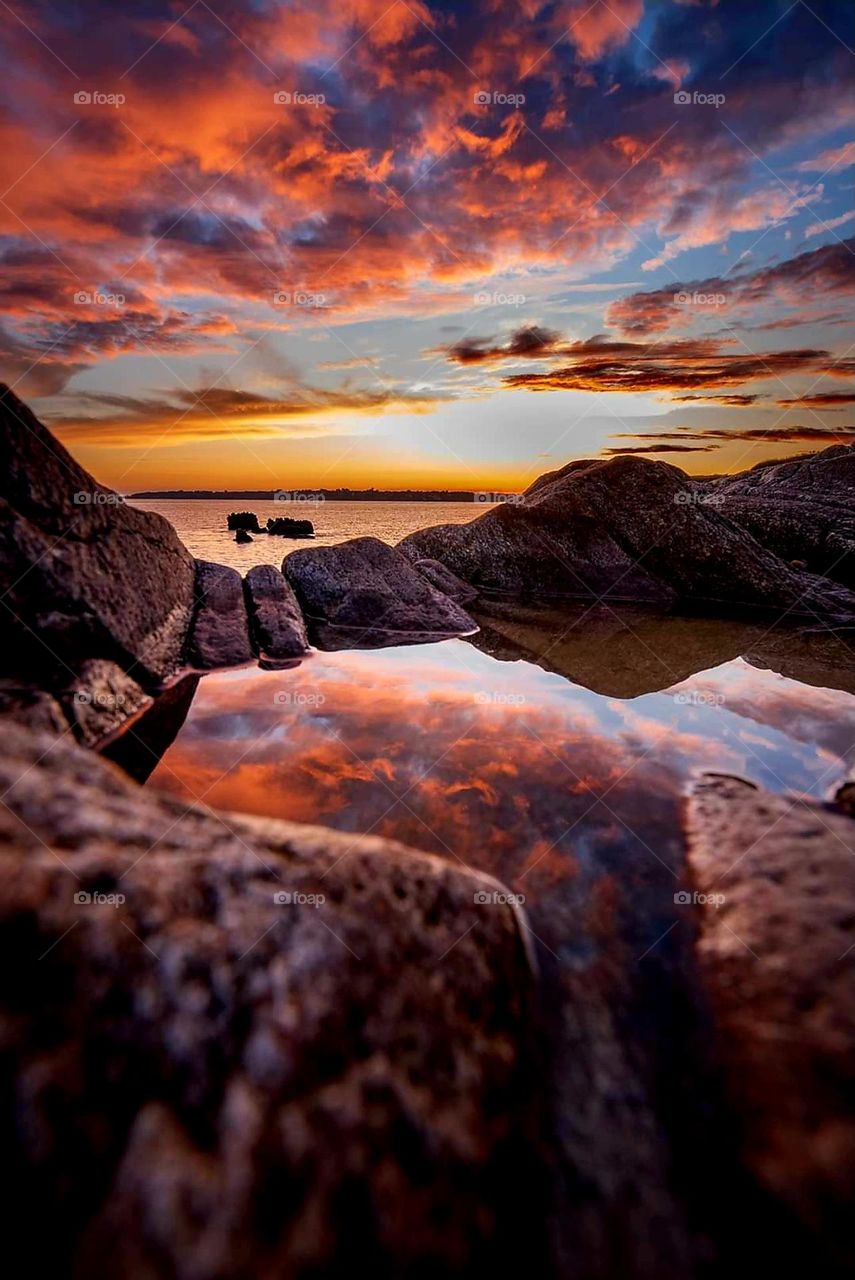 Blue and orange sunrise over the sea and rocks of Moëlan sur Mer reflecting in the waters