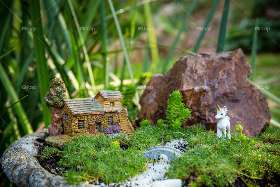 Mini garden pot made in old bird bath for outdoor garden feature. Miniature stone house and unicorn with grass and succulents for trees. Close up miniature outdoor garden