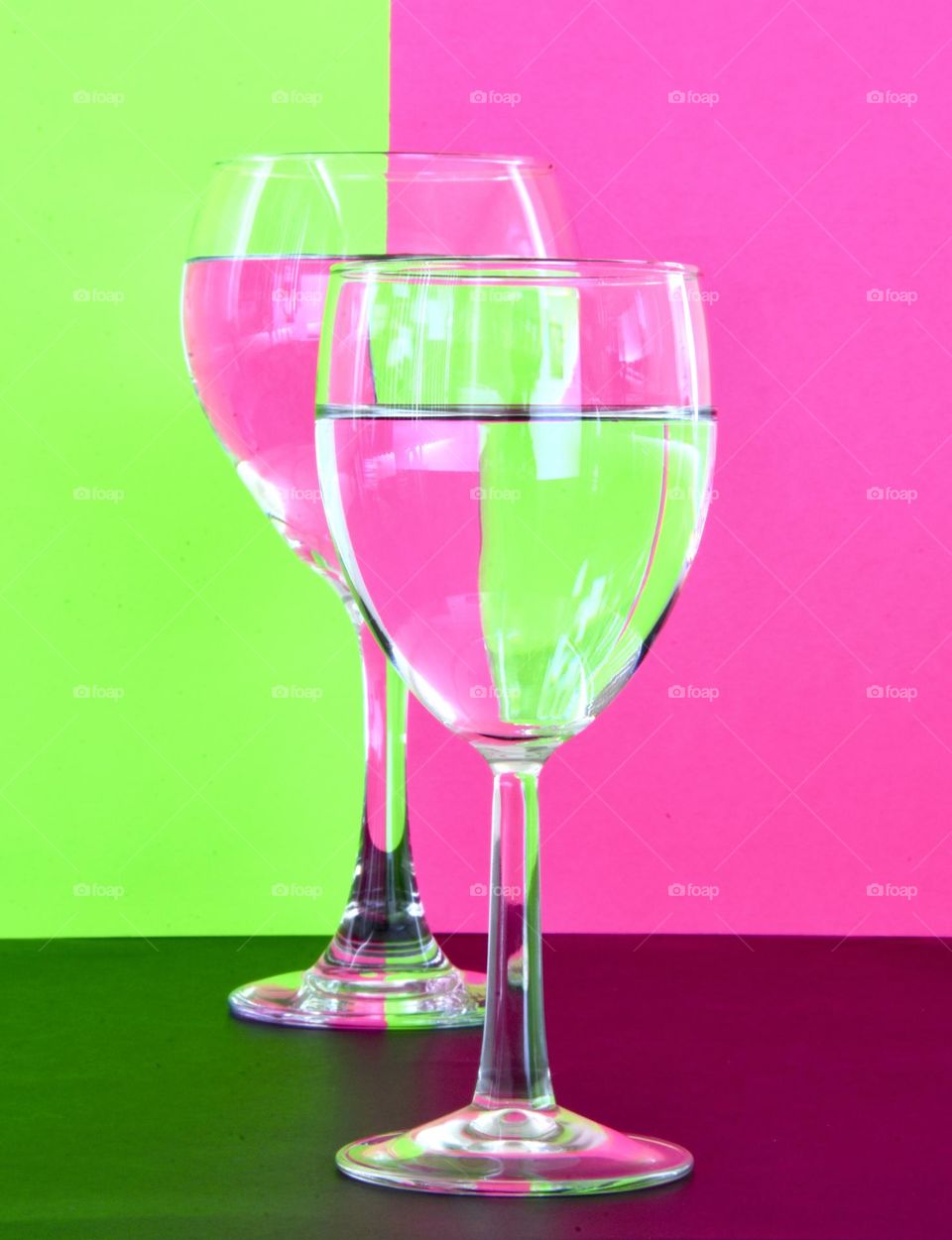 Neon green and neon pink background reflecting into water in wine glasses 