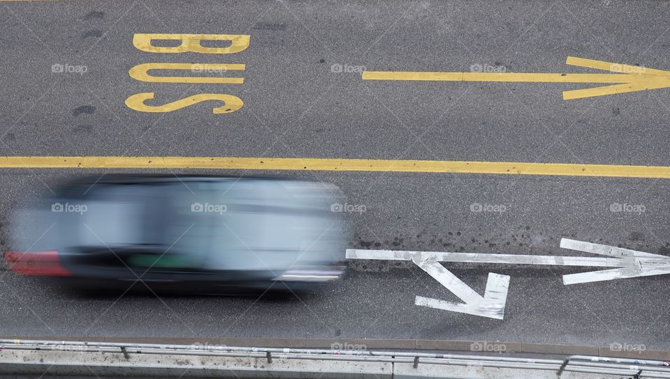 Motion blurred car driving next to bus lane seen from above.
