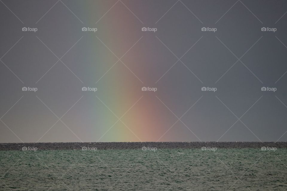 Rainbow arching down through the rain on the ocean horizon during storm 