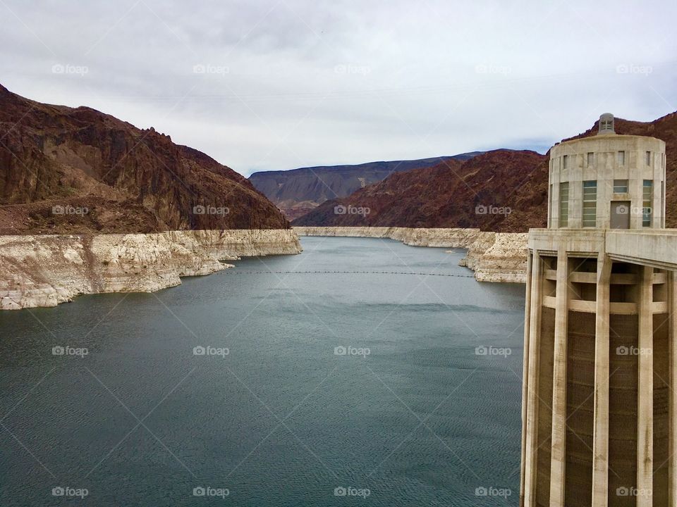 Serene setting from Hoover Dam shows blue, still water flowing between a stunning two-toned mountain landscape