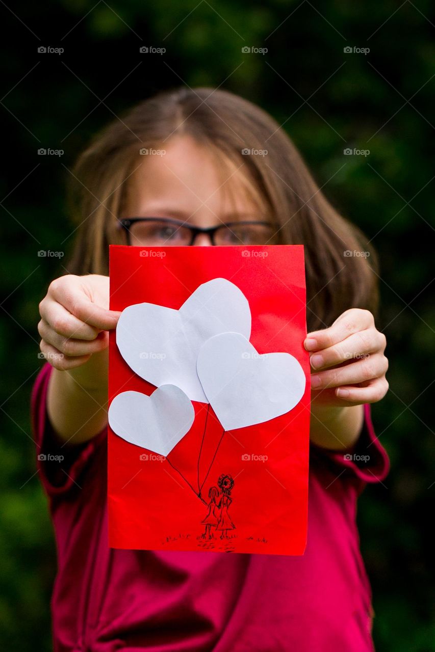 Love, photographed - my mommy loves me. Girl holding handmade card with sketch of mom and daughter. Love balloons.