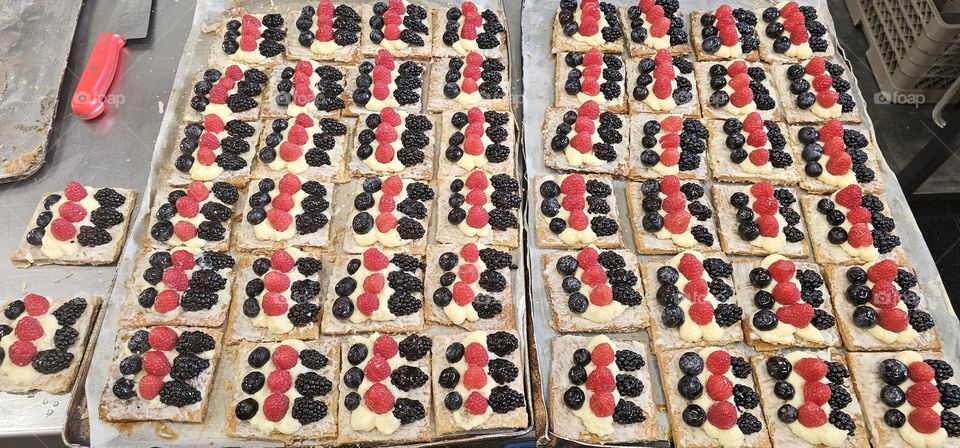 Hojaldre de frutos rojos es hojaldre prensado con azucar se corta por raciones y luego la vase se pinta con chocolate blanco despues por encima la crema pastelera y encima los frutos rojos y por ultimo la gelatina para que brille