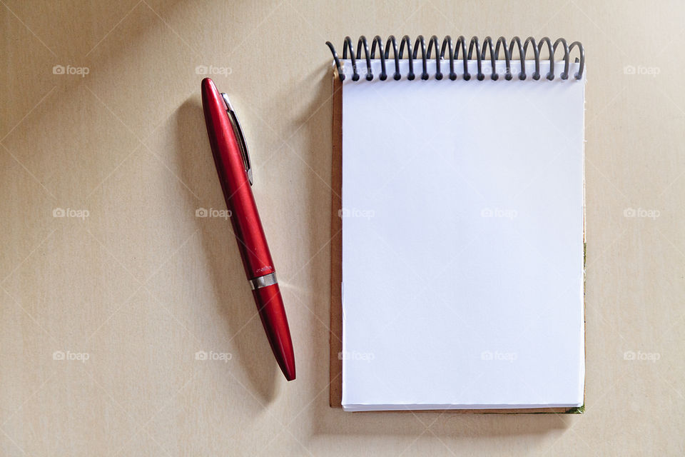 Blank notepad on the wooden table, with a red pen at the side, with sunlight hitting the side. Notepad for noting reminders. Annotation concept. Object concept. Copy space