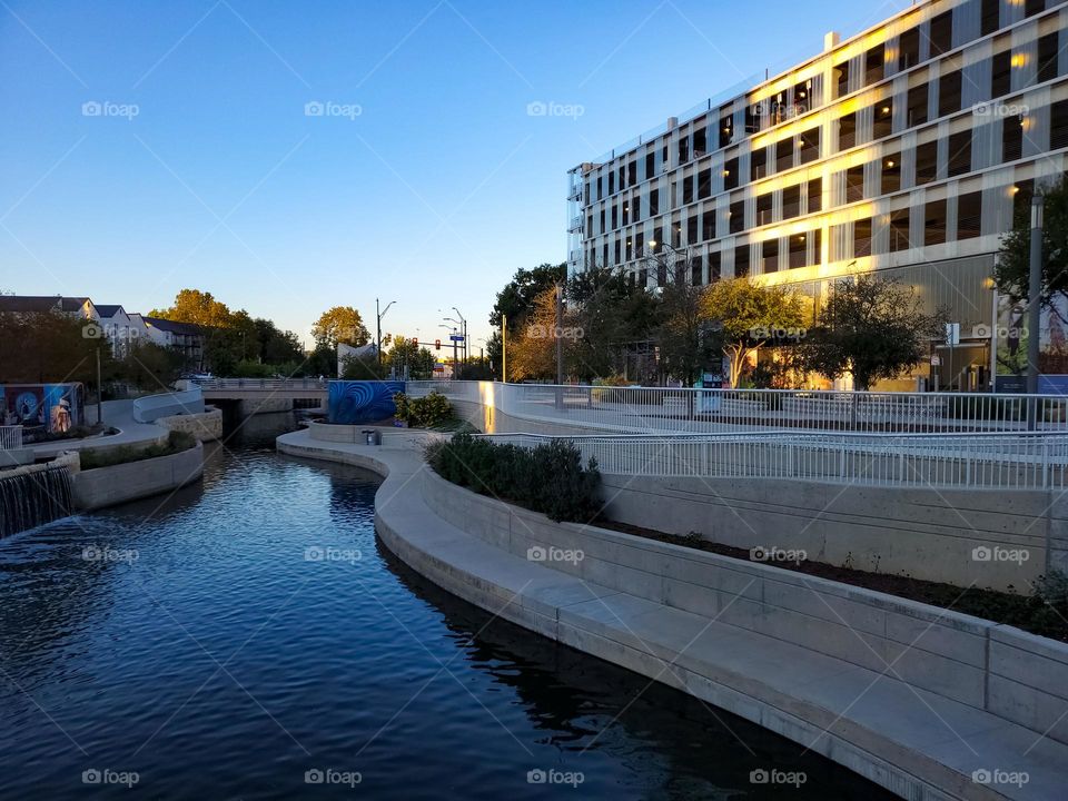 Urban nature waterways - urban river and sidewalk path at sunset with the golden sunlight highlighting a nearby building.