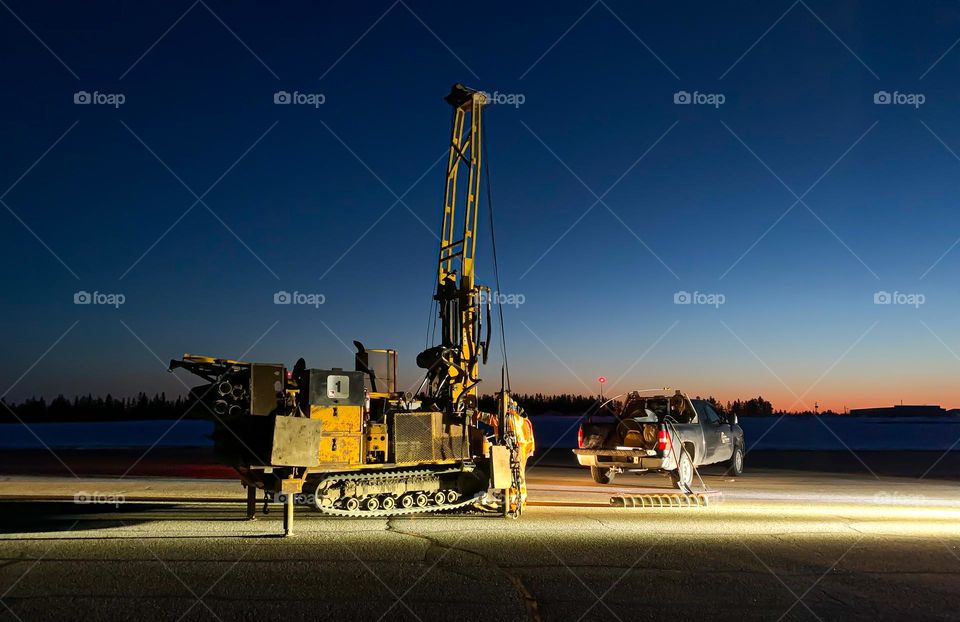 Night drilling works on an airport runway, illuminated by vehicle lights, horizontal 