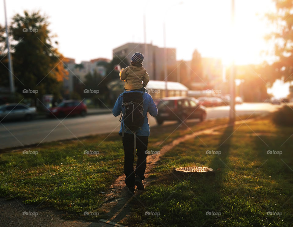 Father and son hiking with a backpack through the autumn city during the golden hour 