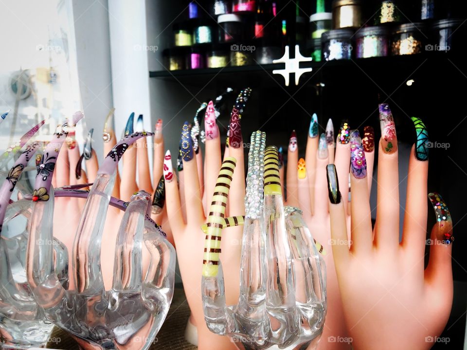 Long nails on female hands, false nails on display in a nail salon’s window, colorful and embellished nails