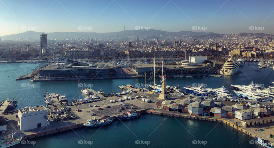 A view from a cable car of boats, the sea, the city and distant mountains at Port Vell, Barcelona