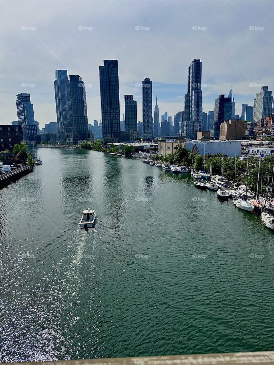 This is “Newtown Creek” with its great variety of boats seen from the “Pulaski Bridge” that connects LIC to “Greenpoint”, Bklyn. Across the “East River” in the distance we see “Manhattan” including the “Empire State Bldg”. 2024. Hypnotic Productions