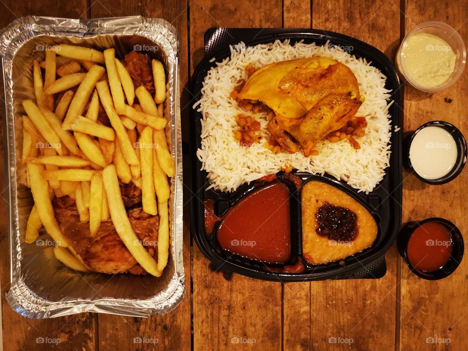 Dinner of white rice, chicken, broast, french fries, sauces and ground garlic