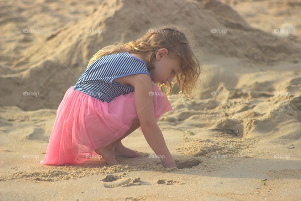 Pretty little girl digging in the sand at the beach. 