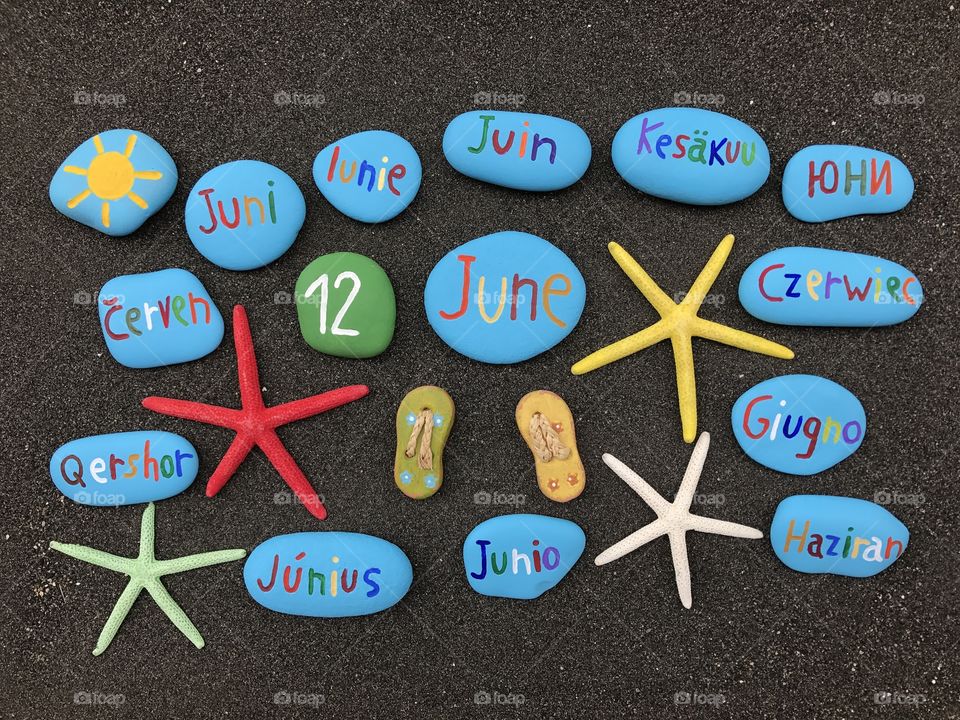 12 June, calendar date with multicolored stones and starfishes over black volcanic sand 